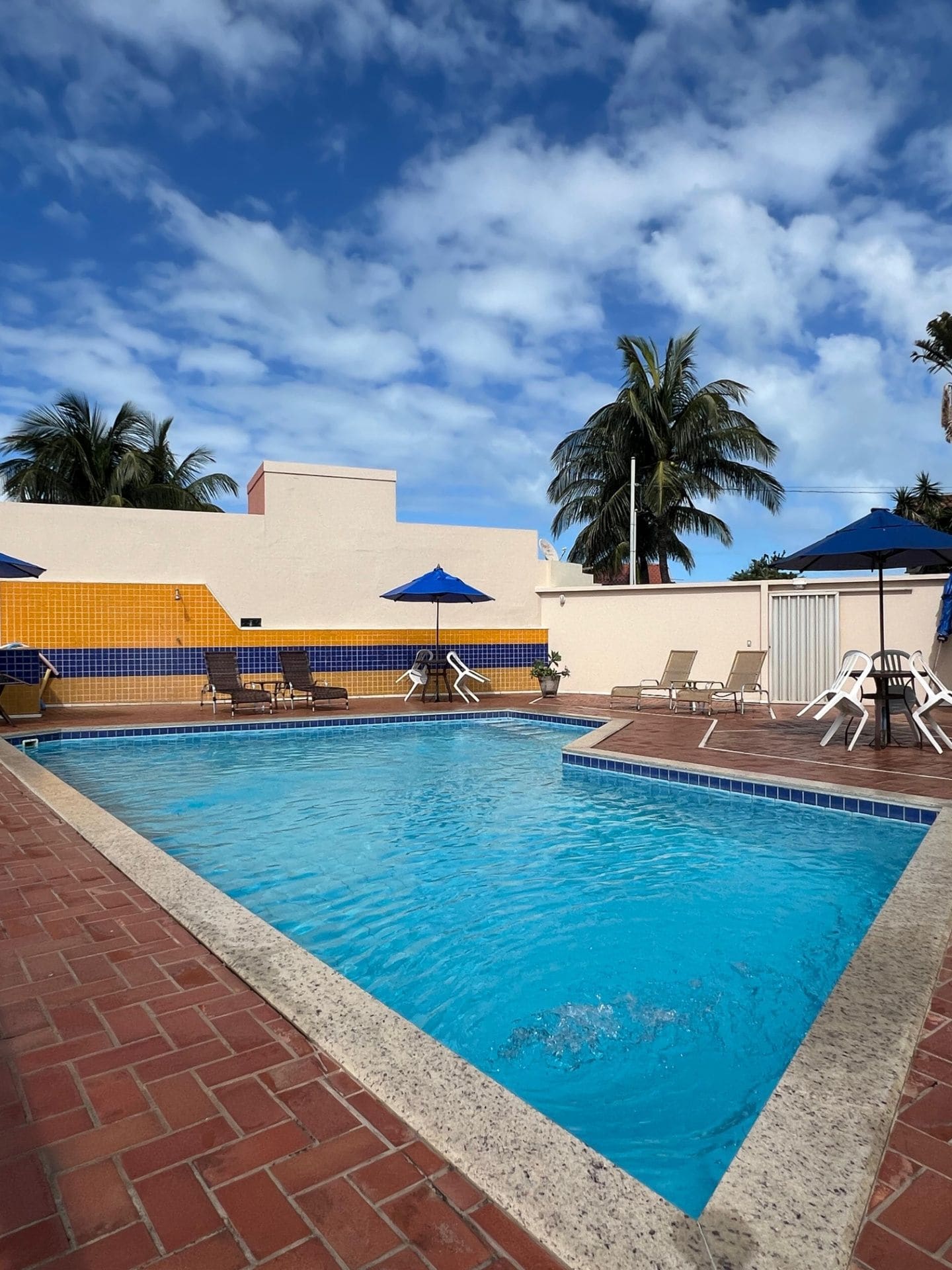 Piscina com guarda-sóis azuis e coqueiros em dia de sol