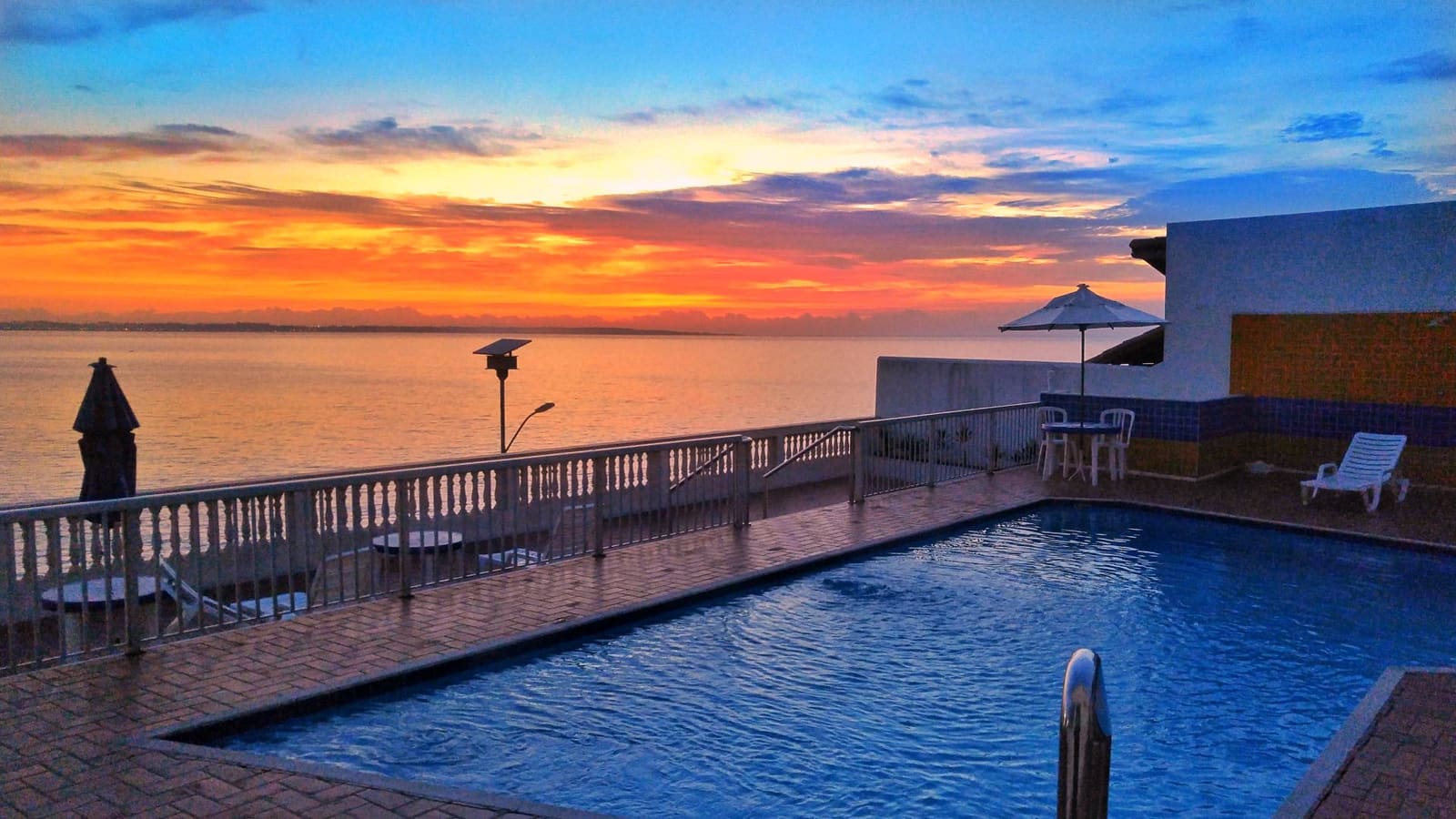 Piscina do hotel ao nascer do sol, com o céu alaranjado sobre o mar