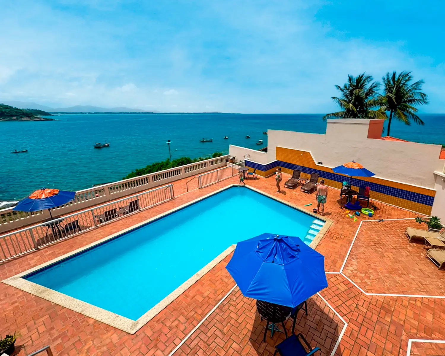 Piscina do hotel com guarda-sóis azuis e vista para o mar da Praia Costa Azul em Iriri